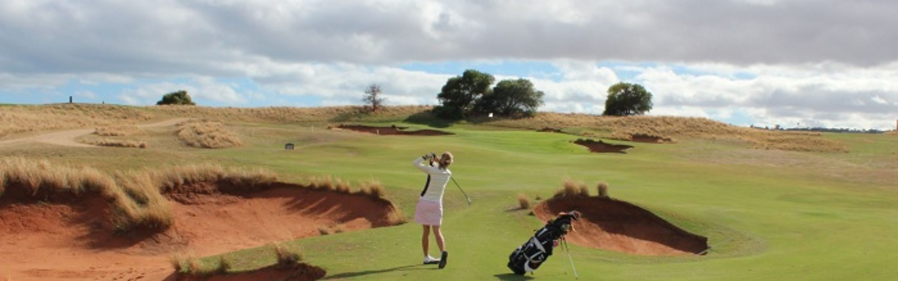 Un campo de golf con búnkeres y árboles al fondo.