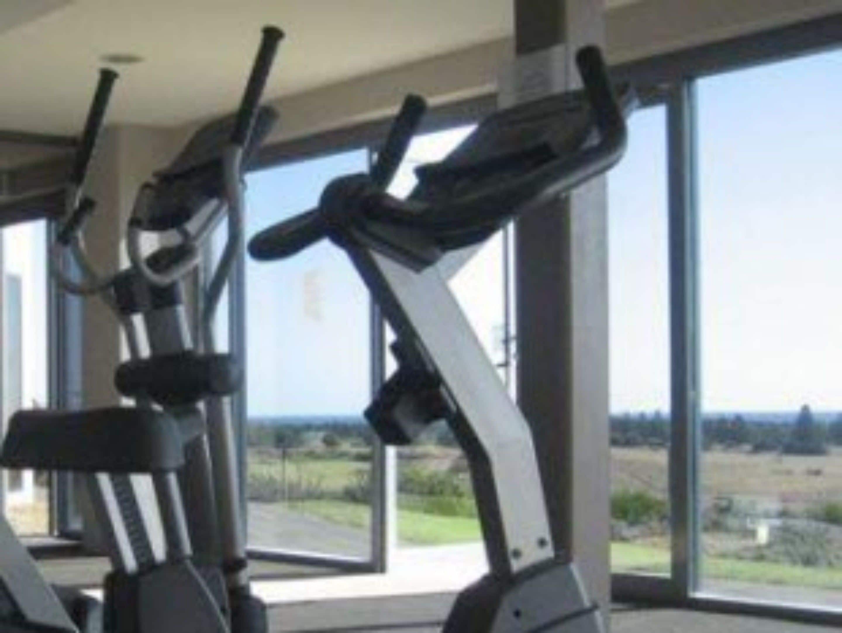 A gym with stationary bikes and large windows offering a view of the outdoors.