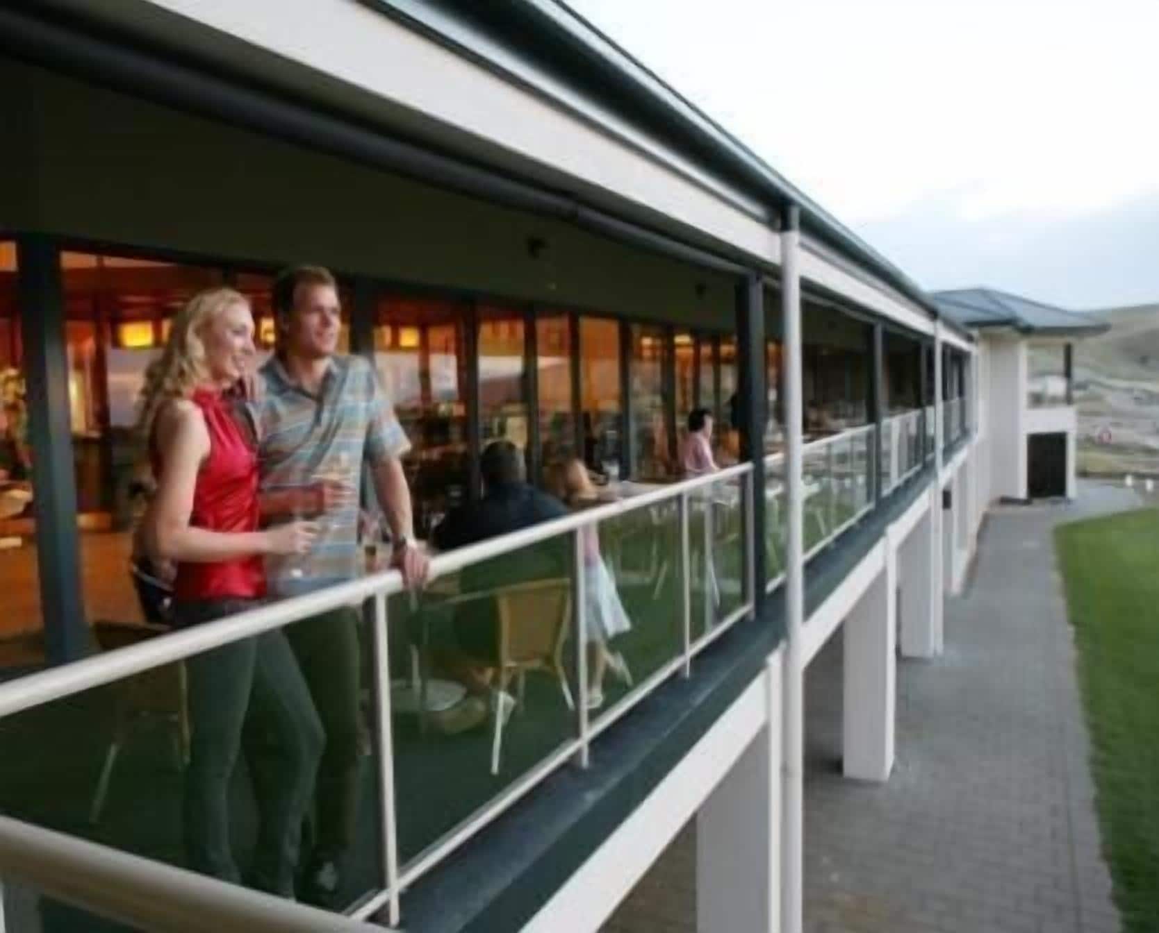 A modern building with a glass balcony overlooking a dining area.