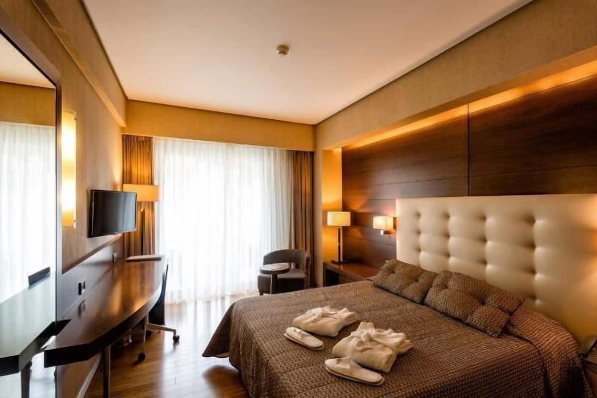 A hotel room with a large bed, a desk, a chair, and a television.