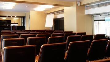 Un salón de conferencias con filas de sillas, una pizarra y una pantalla de proyector.