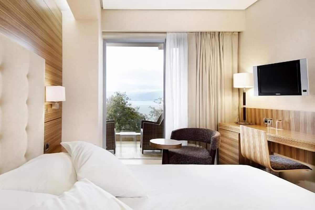 A hotel room with a large bed, a TV, a seating area with a table and chairs, and a view of the outdoors.