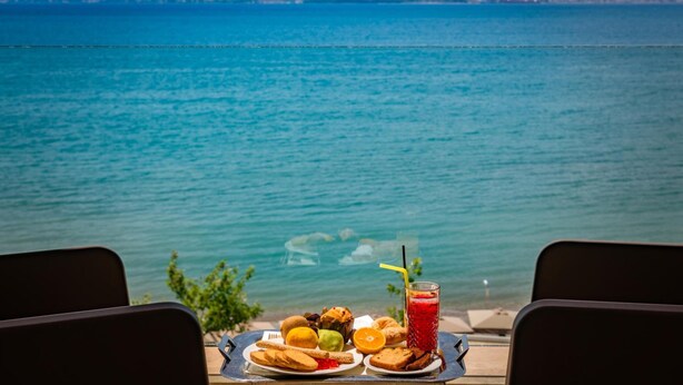 Una mesa con comida y una bebida frente a un lago, con montañas al fondo.