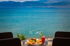 A table with food and a drink by a lake with mountains in the background. - Nafs Hotel (Nafpaktos)
