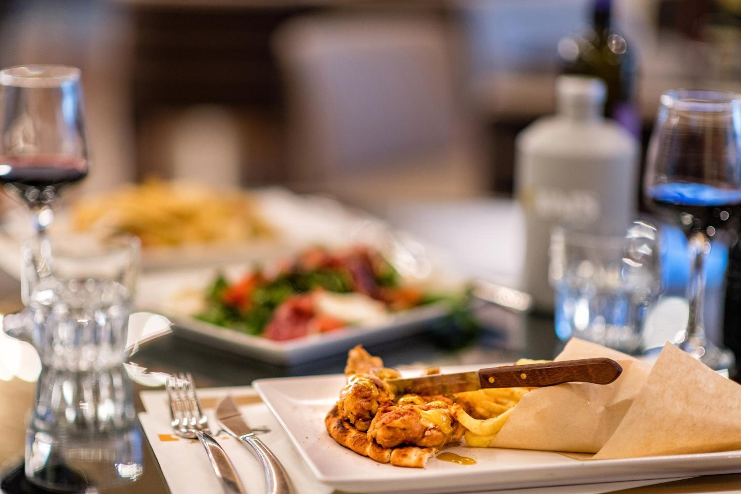 Una mesa de comedor con platos de comida, cubiertos y copas de vino.