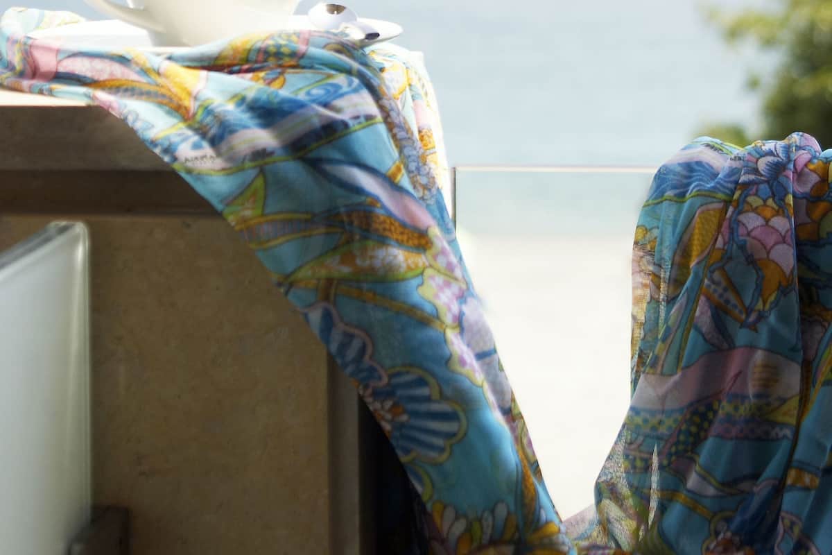 A white cup on a table with a colorful cloth, overlooking a body of water and distant mountains.