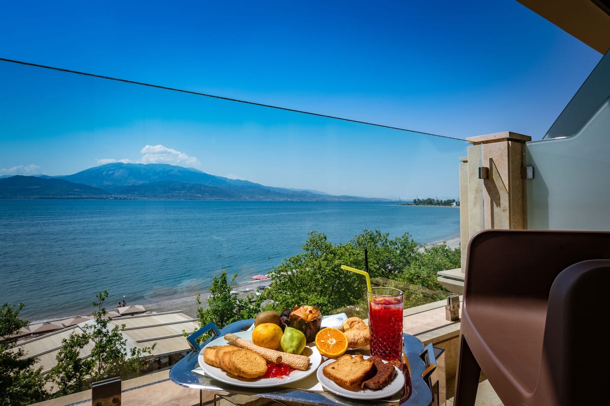 A table with food and a drink, overlooking a lake and mountains.