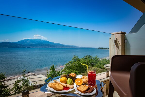 A table with food and a drink, overlooking a lake and mountains.