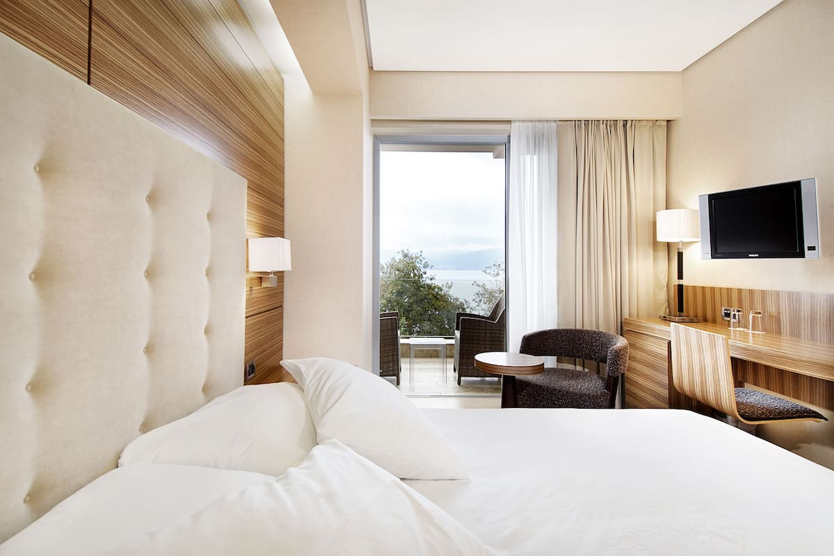 A hotel room with a large bed, a television, a small table, and a view of the outdoors.