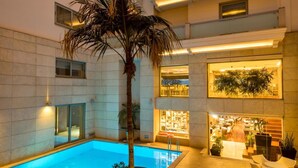 Un hotel moderno con piscina, mobiliario exterior y un atrio bien iluminado.