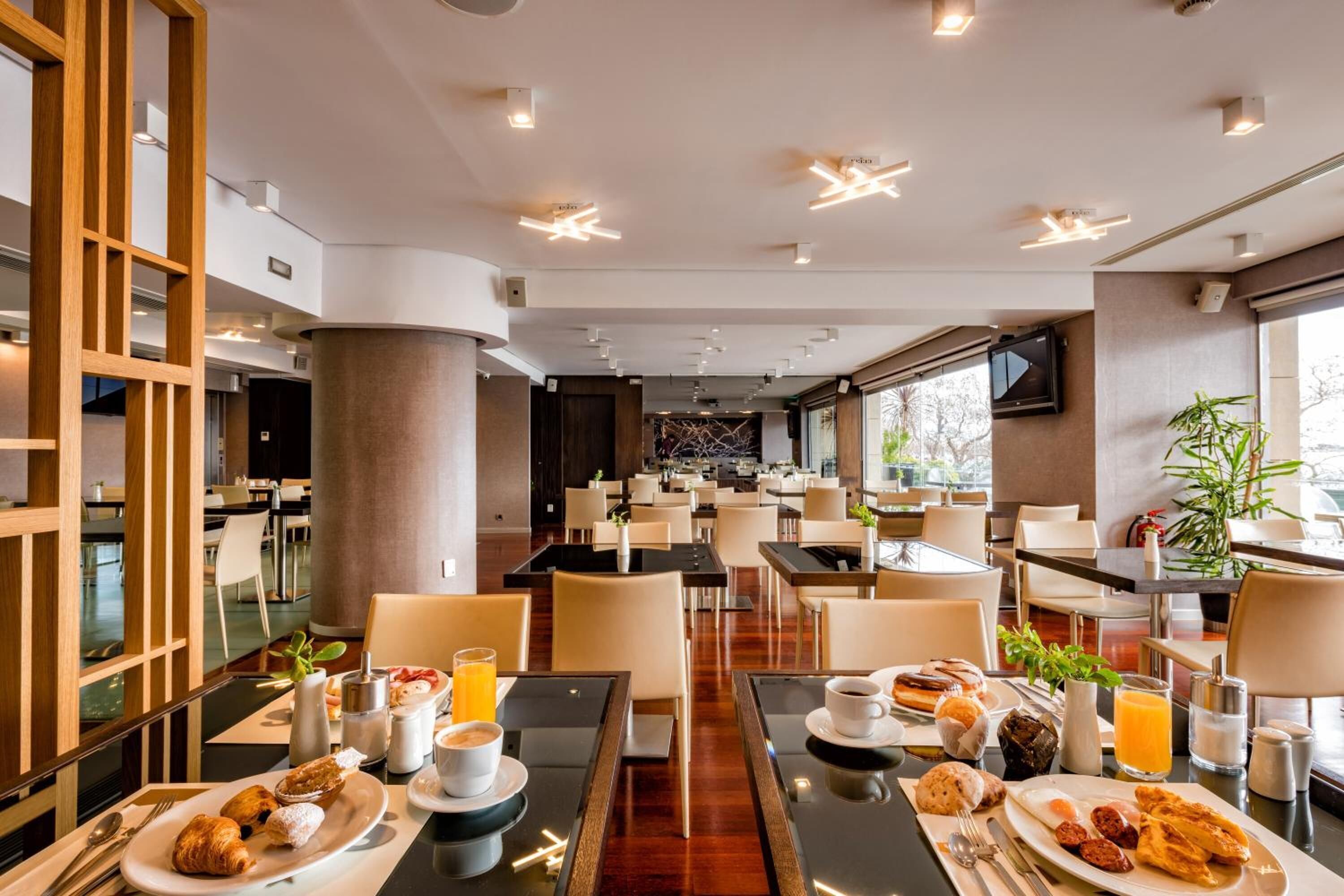 Un espace repas moderne dans un hôtel, avec des tables préparées pour le petit-déjeuner, où l’on trouve des croissants, des œufs et du jus d’orange.