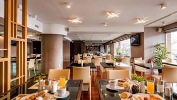 Un espace repas moderne dans un hôtel, avec des tables préparées pour le petit-déjeuner, où l’on trouve des croissants, des œufs et du jus d’orange.