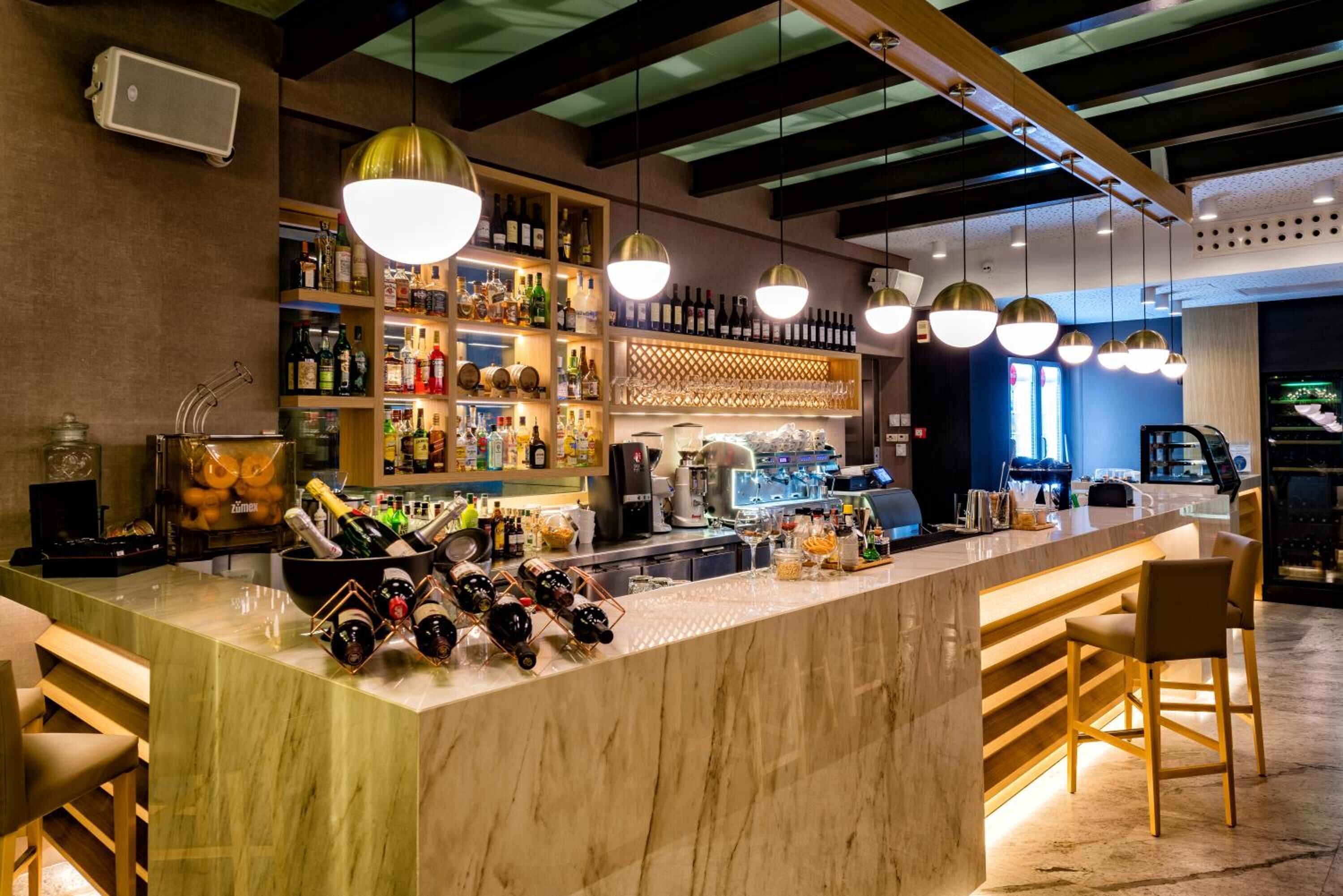 Zona bar con un bancone in marmo, scaffali pieni di bottiglie e lampade a sospensione.