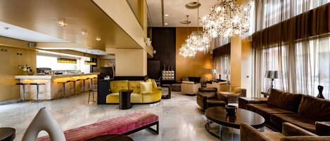 A spacious hotel lobby with a bar area, seating arrangements, and a chandelier.