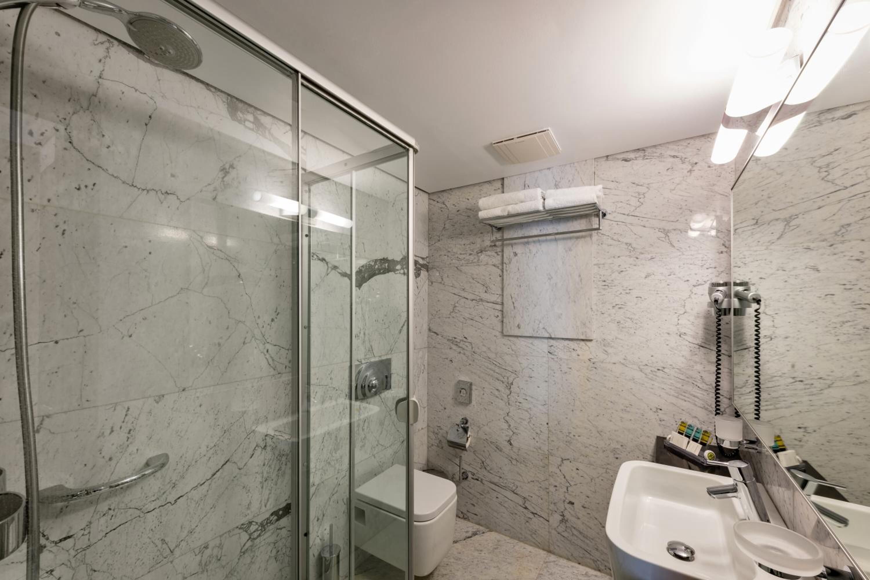 Un baño moderno con ducha envuelta en vidrio, inodoro blanco y lavamanos con espejo.