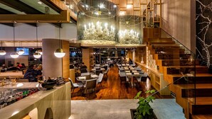Un restaurante espacioso con techos altos, candelabros modernos y una escalera central.