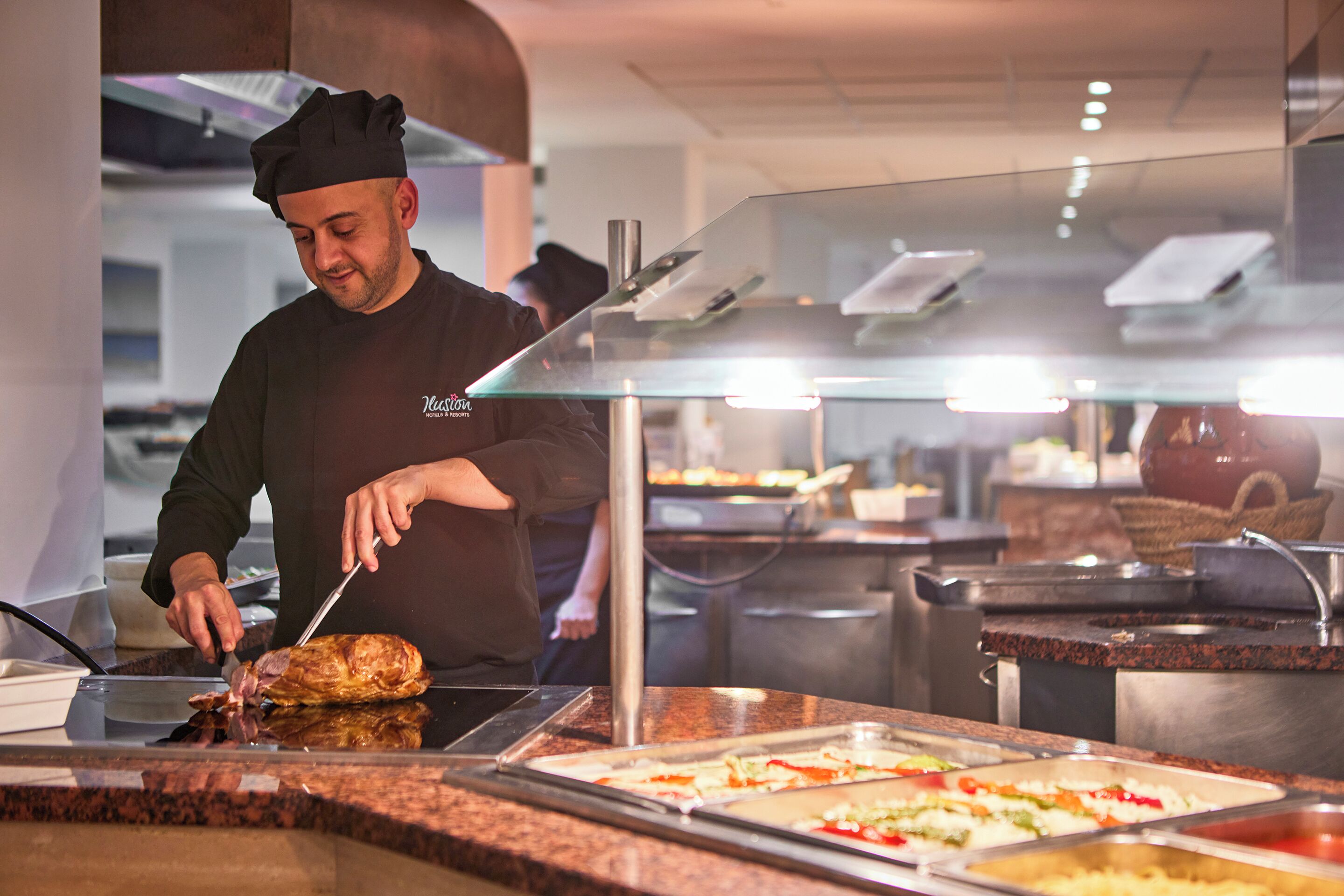 A chef preparing food in a commercial kitchen with stainless steel appliances and buffet-style food service.