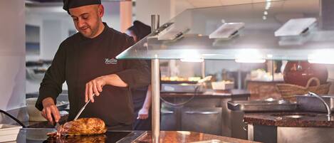 A chef preparing food in a commercial kitchen with stainless steel appliances and buffet-style food service.