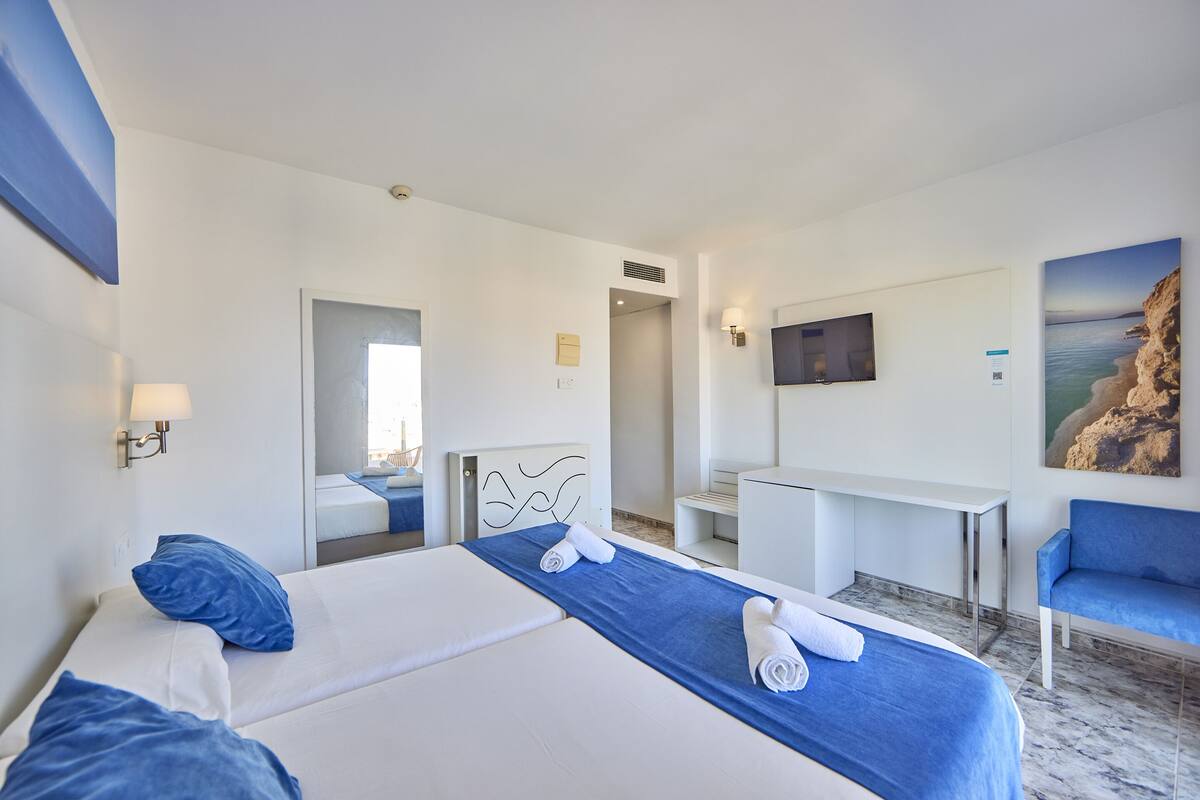 Une chambre d’hôtel avec un grand lit, un bureau, une télévision et un tableau représentant un paysage côtier.