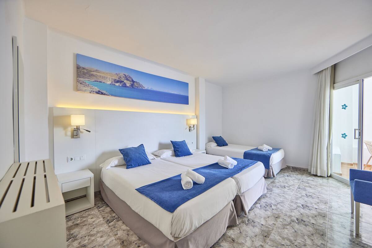 Une chambre d’hôtel avec deux lits, un tableau représentant un paysage côtier, une petite table et une chaise.