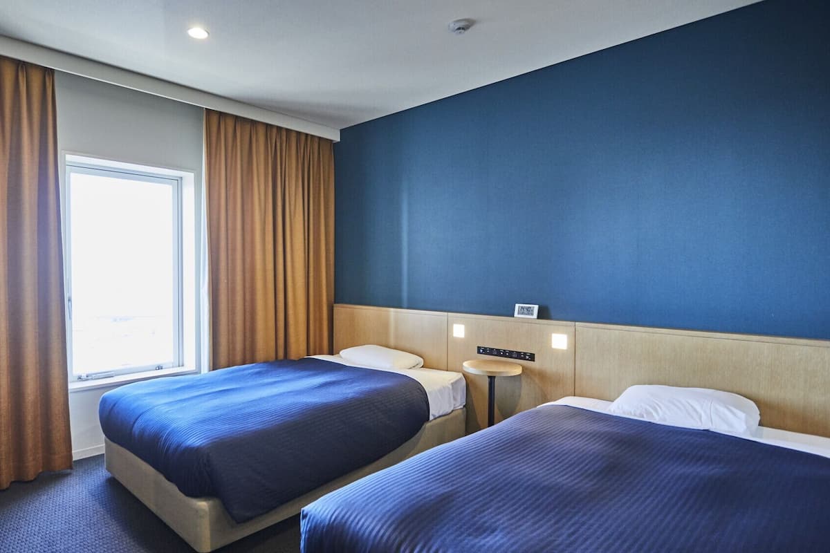 Een hotelkamer met twee bedden, een raam en een wandklok.