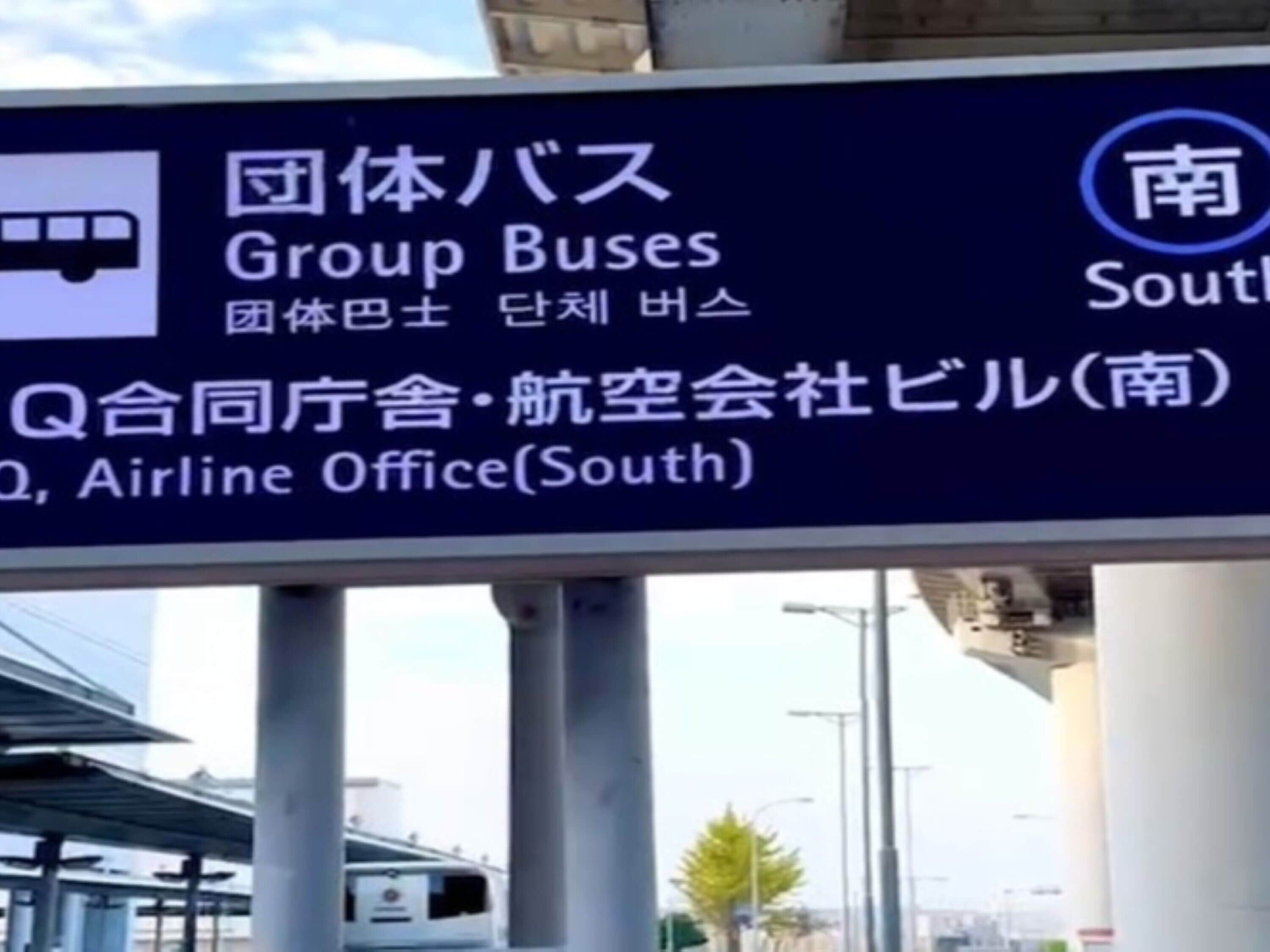 A sign with directions to Group Buses, Airline Office, and Q, with Japanese text.