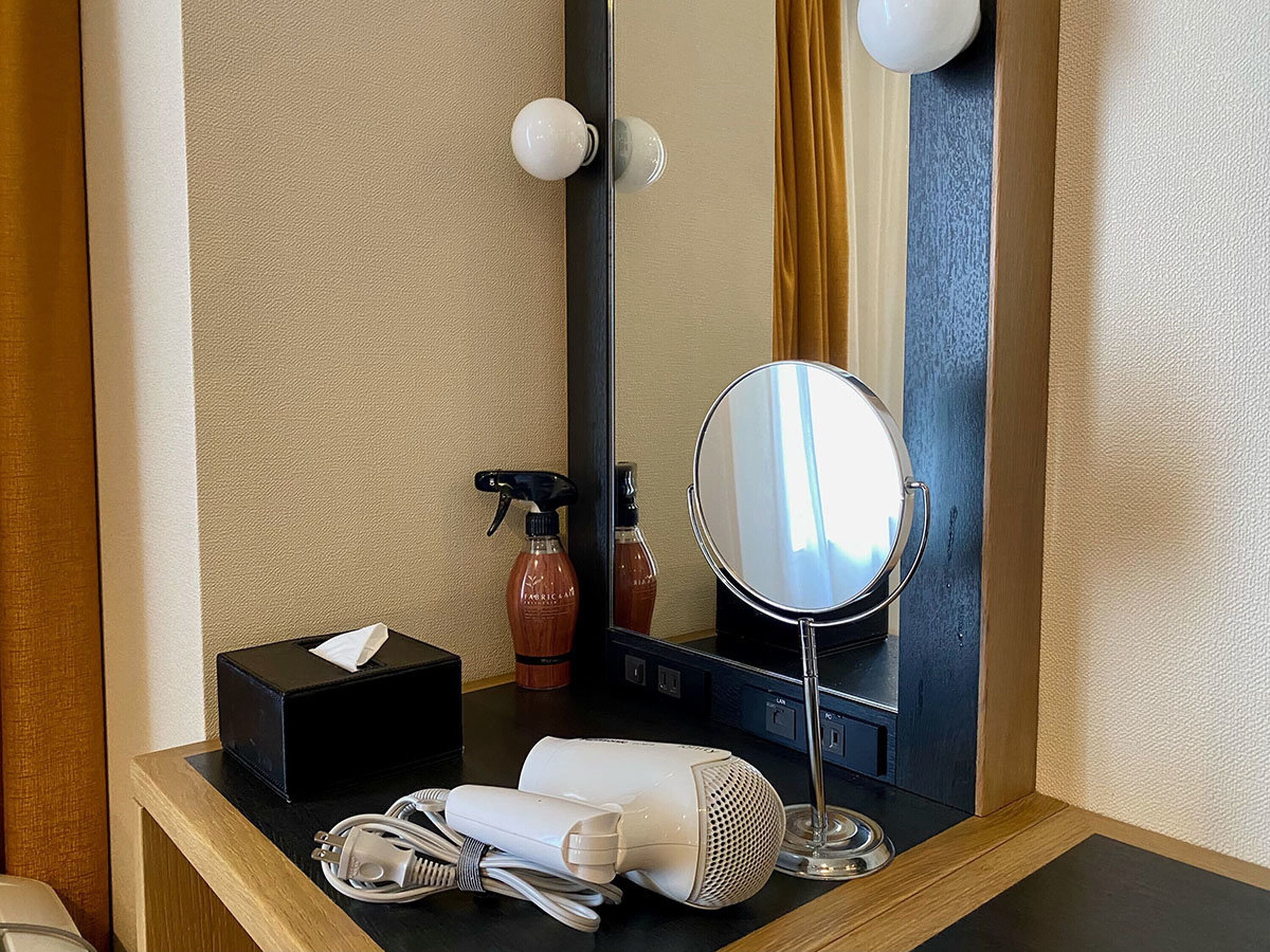 A hotel bathroom with a vanity, a mirror, a hairdryer, and toiletries.