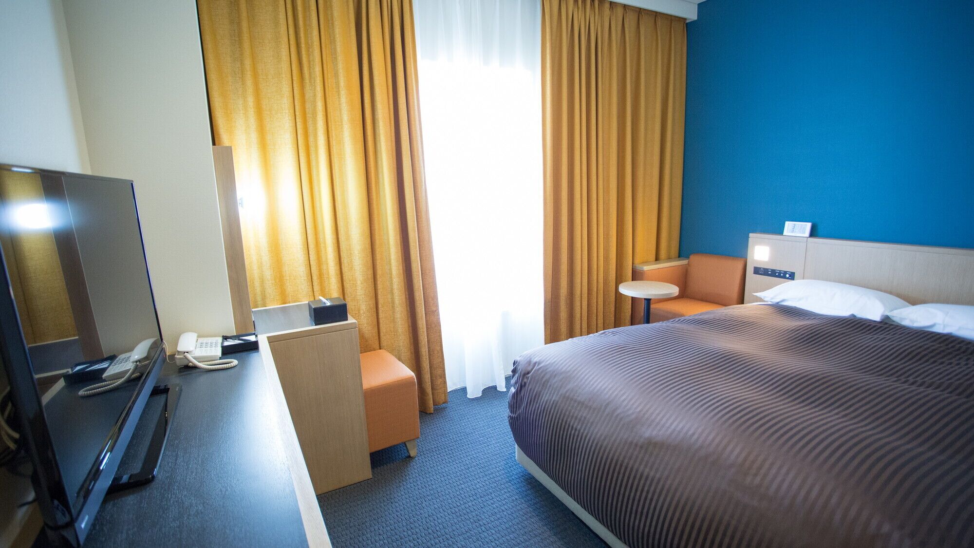 Une chambre d’hôtel comprenant un lit, un bureau avec un téléphone, une chaise, une petite table et un téléviseur.