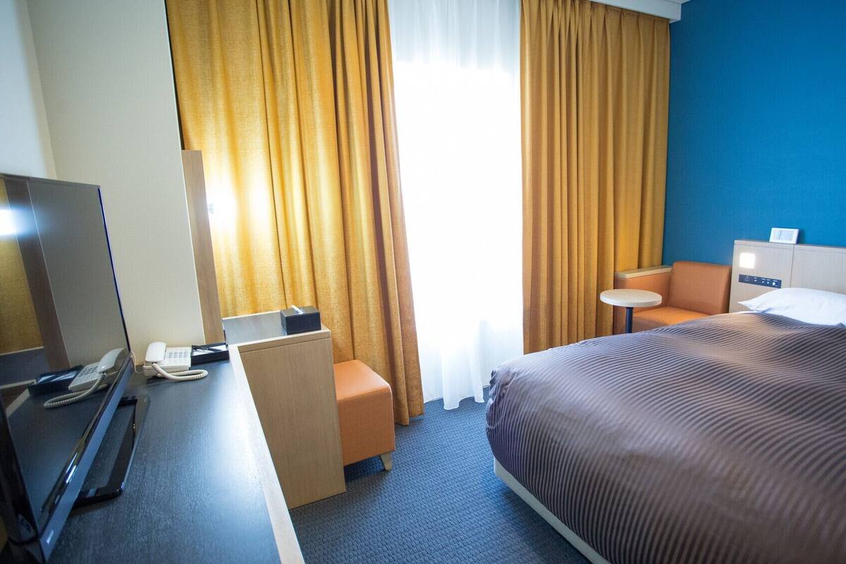 Een hotelkamer met een bed, een bureau met telefoon, een stoel, een kleine tafel en een televisie.