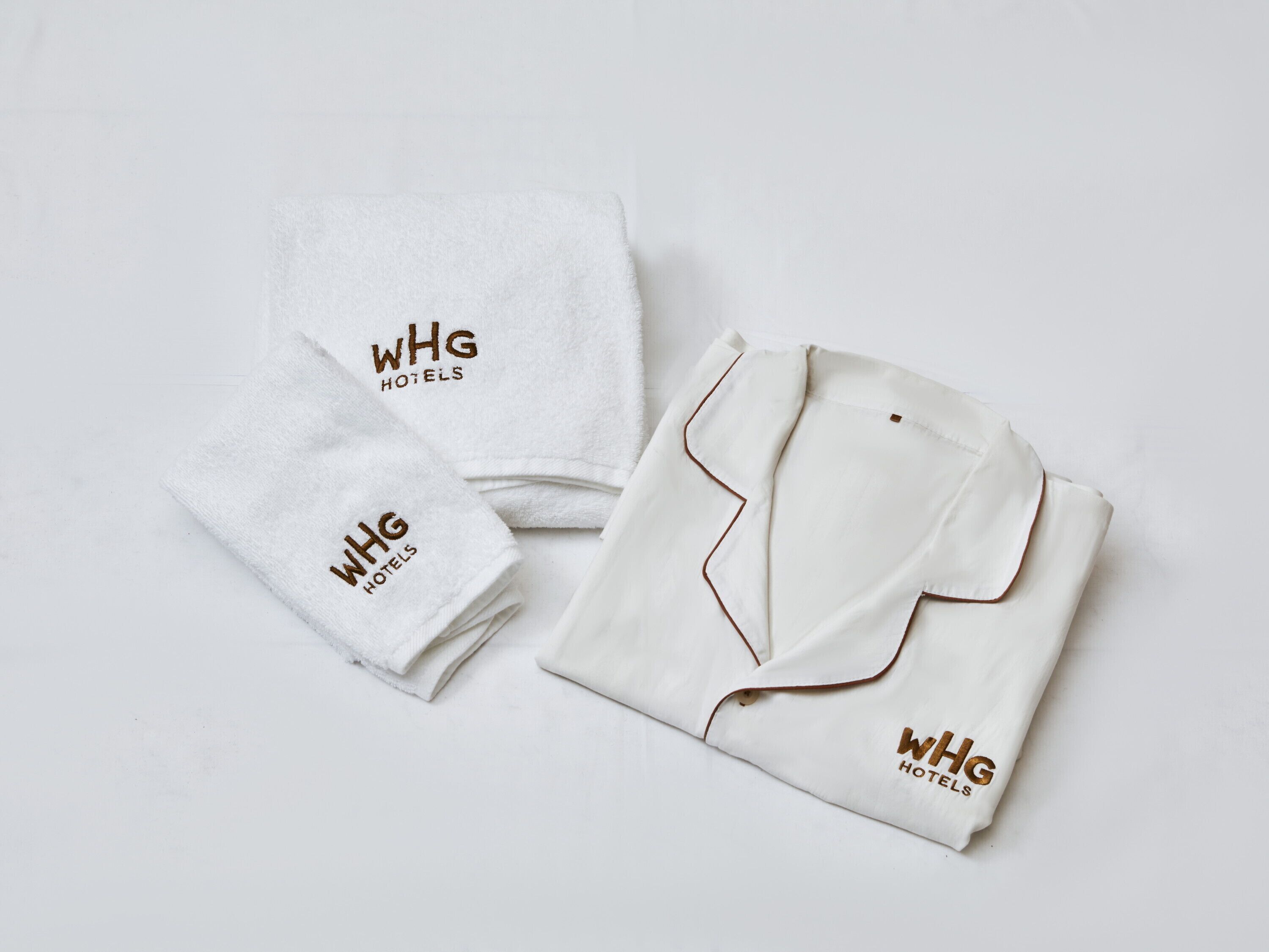 Una camisa blanca doblada con cuidado y dos toallas blancas con el logo de WHG Hotels.