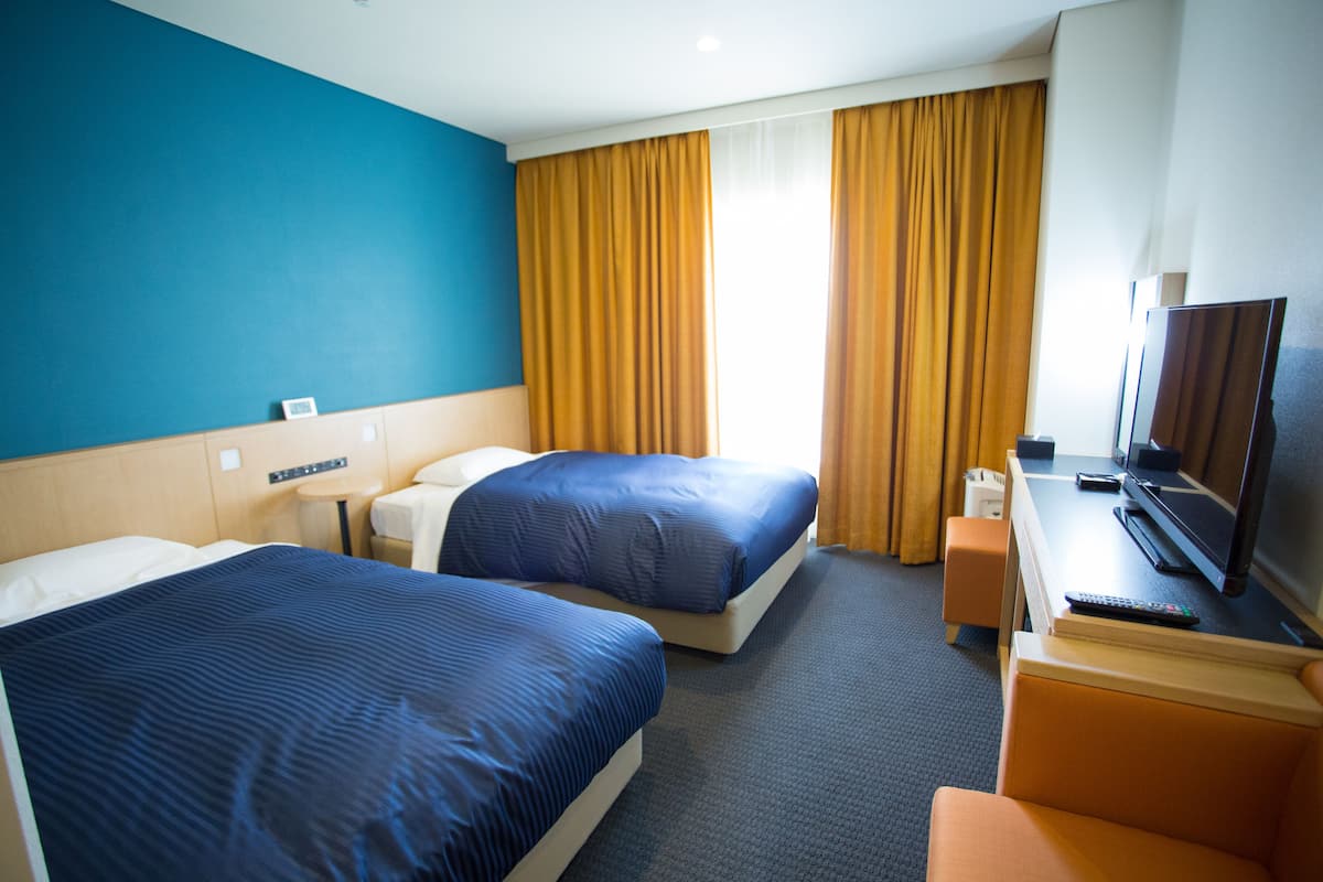 Een hotelkamer met twee bedden, een bureau met een televisie en een raam met gordijnen.