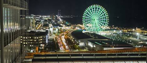 A nighttime cityscape with a prominent Ferris wheel, modern buildings, and a busy highway.