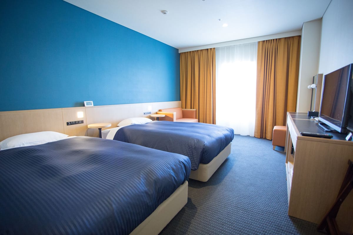 Een hotelkamer met twee bedden, een bureau met een televisie, een klein tafeltje en een stoel.
