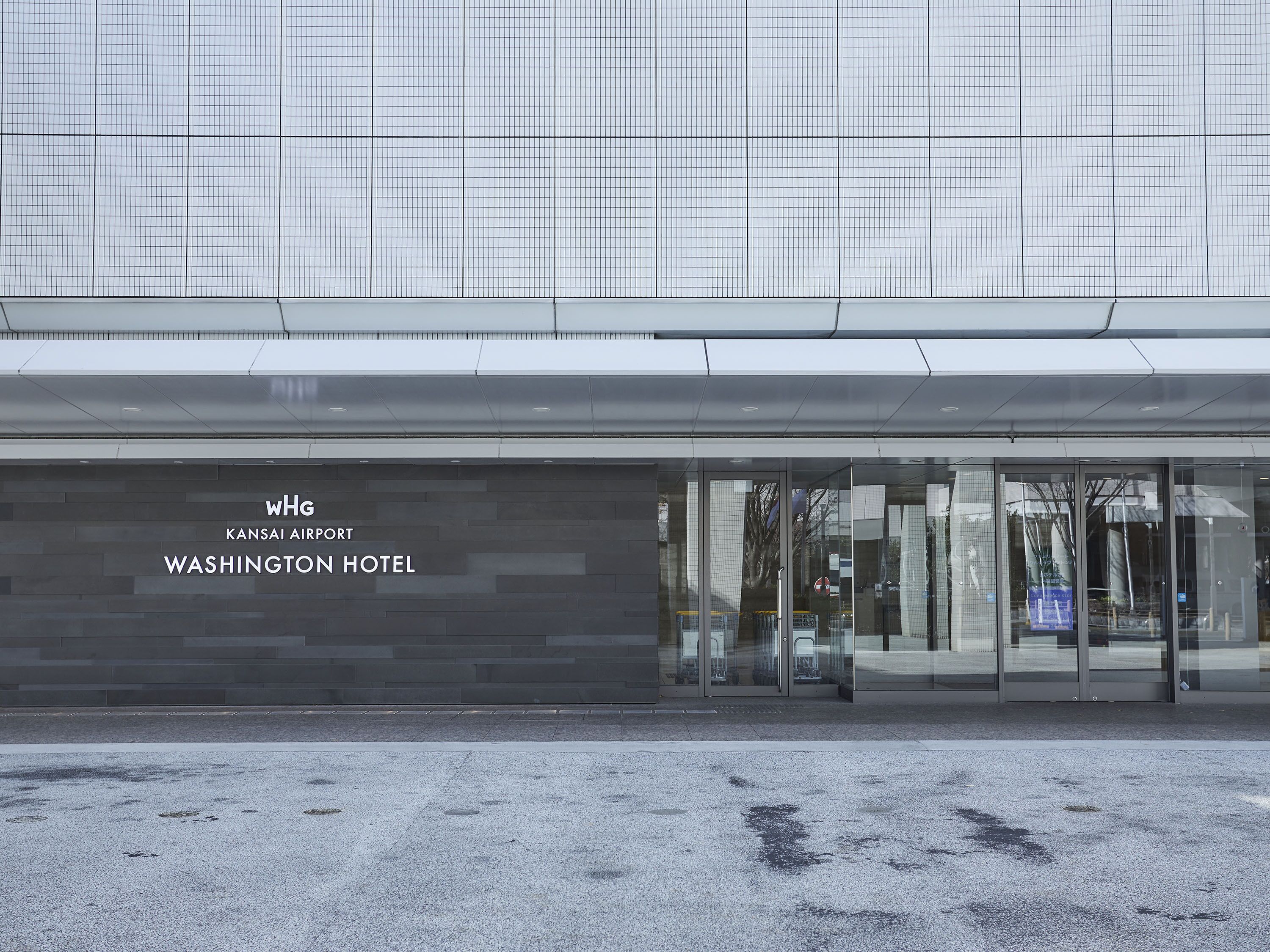 Un bâtiment moderne doté d’une façade en verre et d’une enseigne indiquant : « WHG KANSAI AIRPORT WASHINGTON HOTEL ».