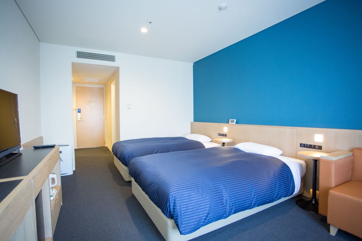 Een hotelkamer met twee bedden, een bureau met televisie, een nachtkastje met lamp en een zithoekje.