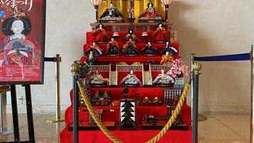 A display of traditional Japanese dolls and artifacts on a red carpet, with a golden rope barrier in front.