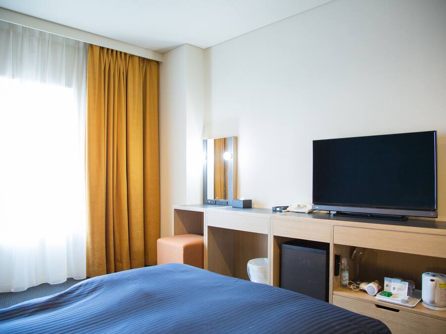 Een hotelkamer met een bed, een bureau met een televisie, een koffiezetapparaat en een prullenbak.