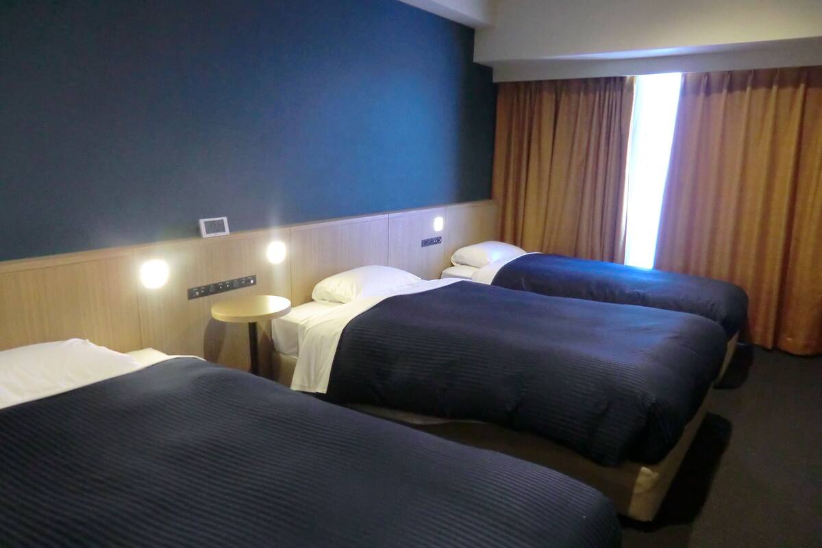 Een hotelkamer met twee eenpersoonsbedden, een klein rond tafeltje en een raam met gordijnen.
