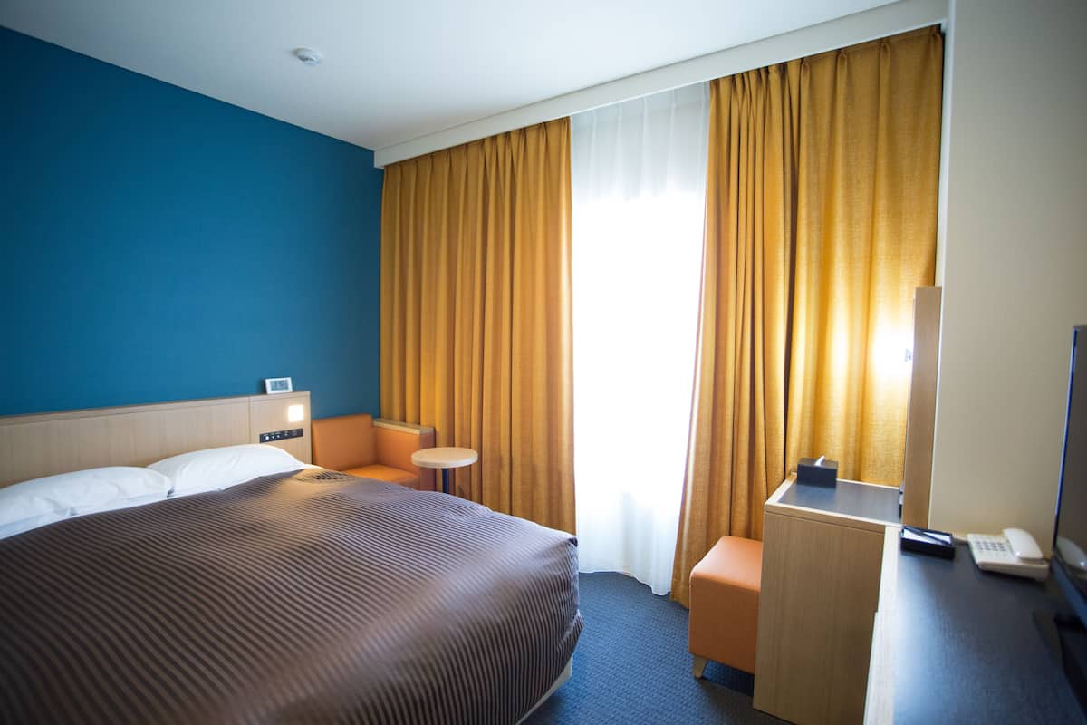 Een hotelkamer met een groot bed, een bureau met telefoon, een klein tafeltje en een stoel.