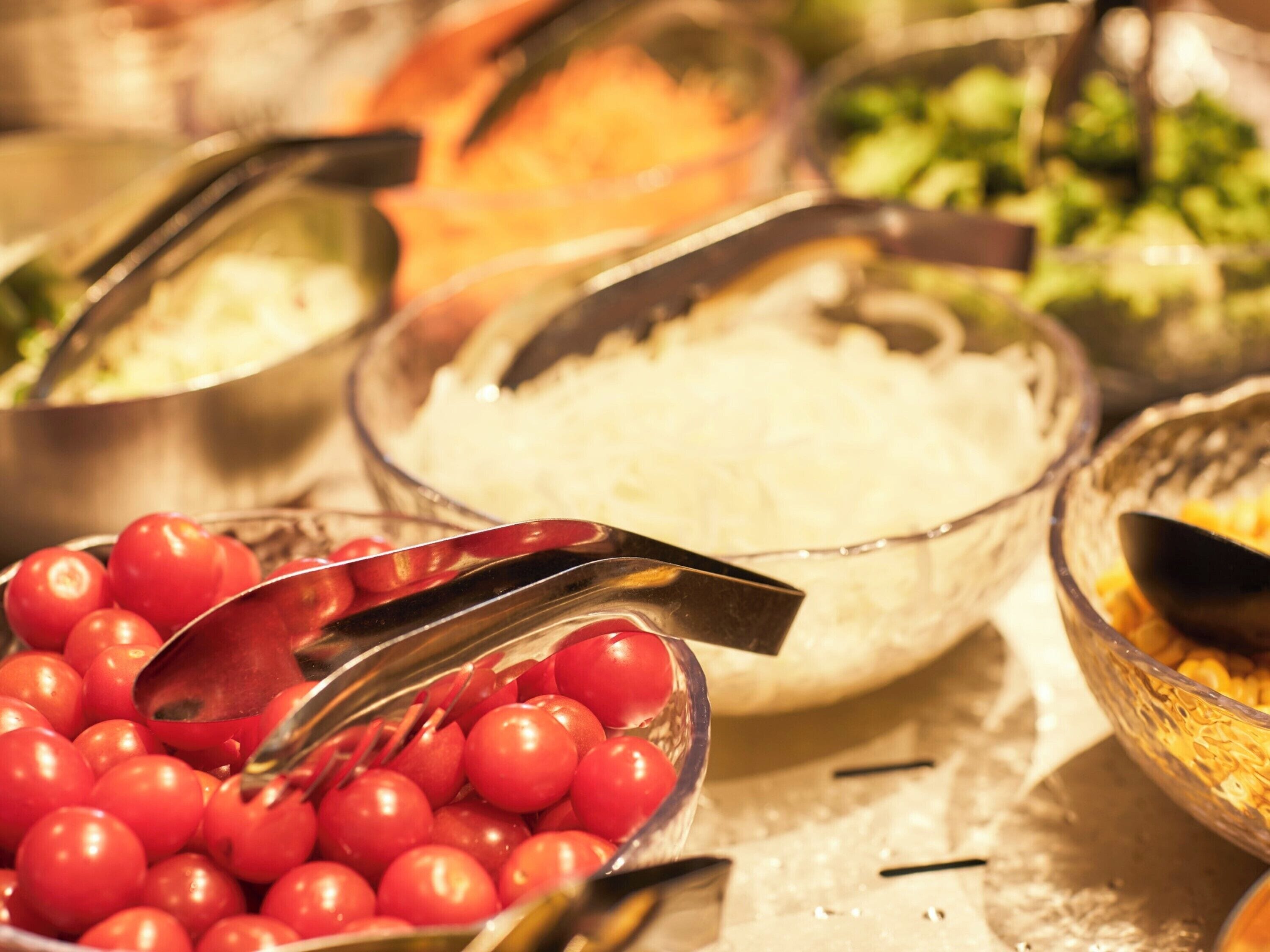 Een buffet met diverse gerechten, waaronder een kom rode tomaten, een kom rijst en andere maaltijden.