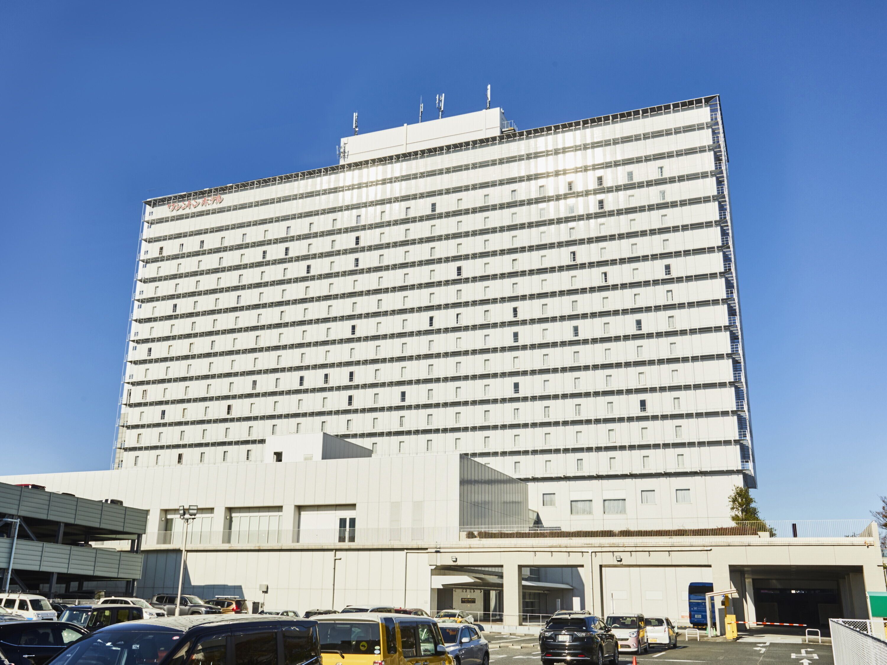 Un hotel grande de varios pisos con un diseño arquitectónico moderno, que cuenta con una entrada destacada y un área de estacionamiento al frente.