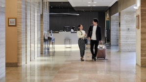 Een moderne hotellobby met een receptiebalie, een zithoek en een duidelijke doorgang voor gasten.
