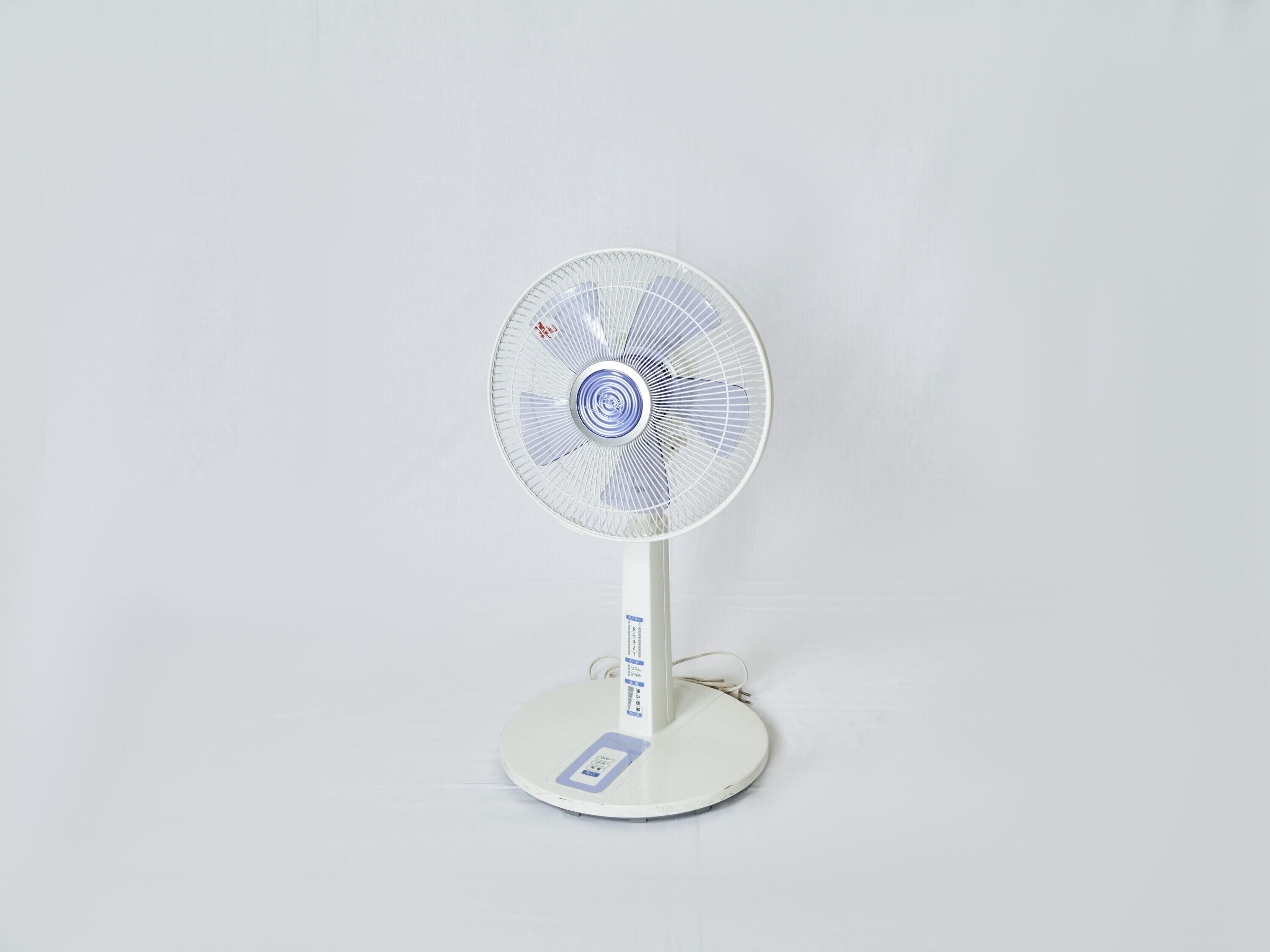 A standing electric fan with a white base and a circular design.