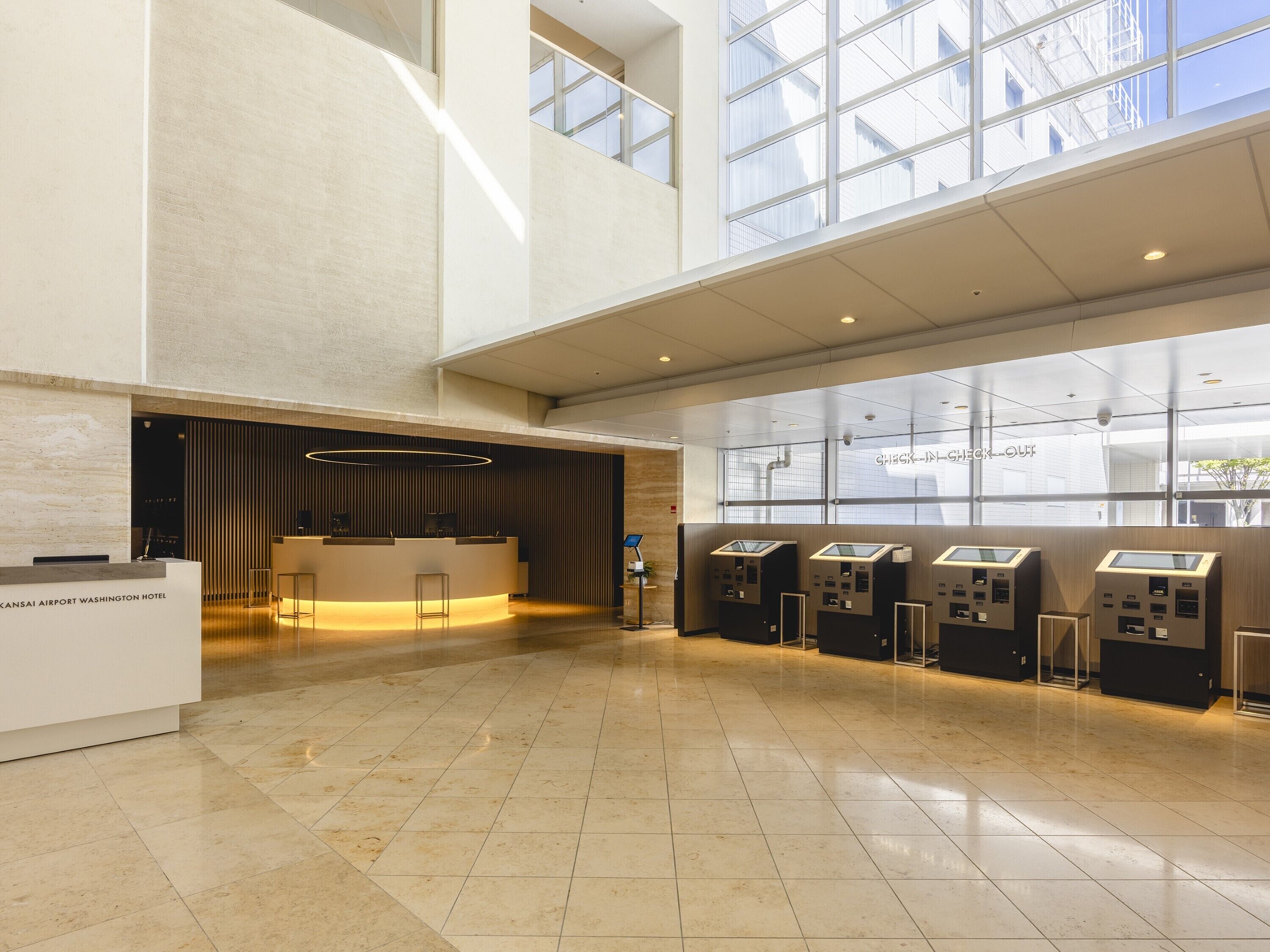 A spacious lobby with a reception desk, check-in kiosks, and large windows offering views of the building's exterior.