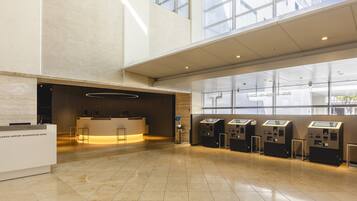 A spacious lobby with a reception desk, check-in kiosks, and large windows offering views of the building's exterior.