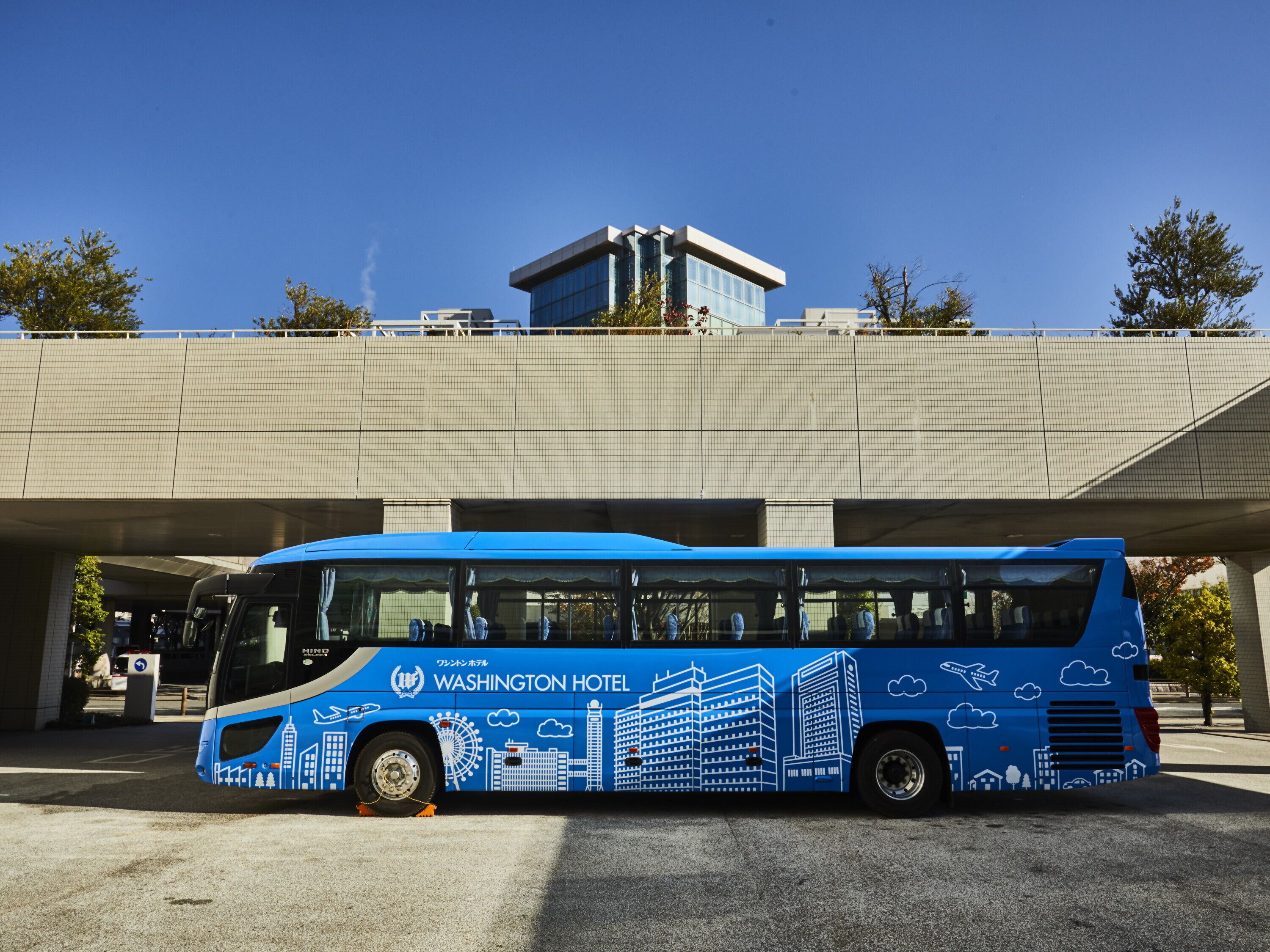 Een blauwe bus met de branding van het Washington Hotel geparkeerd onder een viaduct.