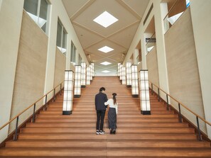 Una escalera con escalones de madera y barandillas negras, flanqueada por paredes con amplias ventanas e iluminada por lámparas modernas.