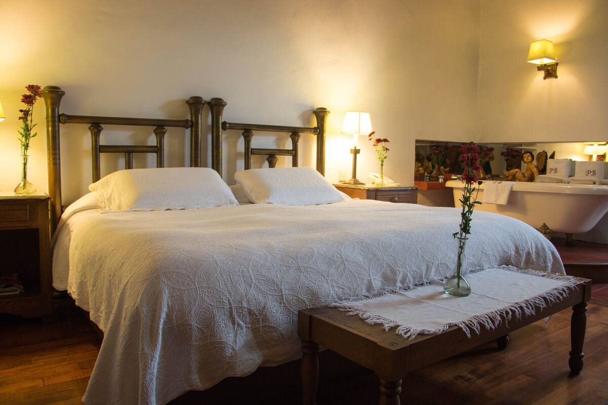 A large bed with a wooden headboard, a bedside table with a lamp, and a vase with flowers.