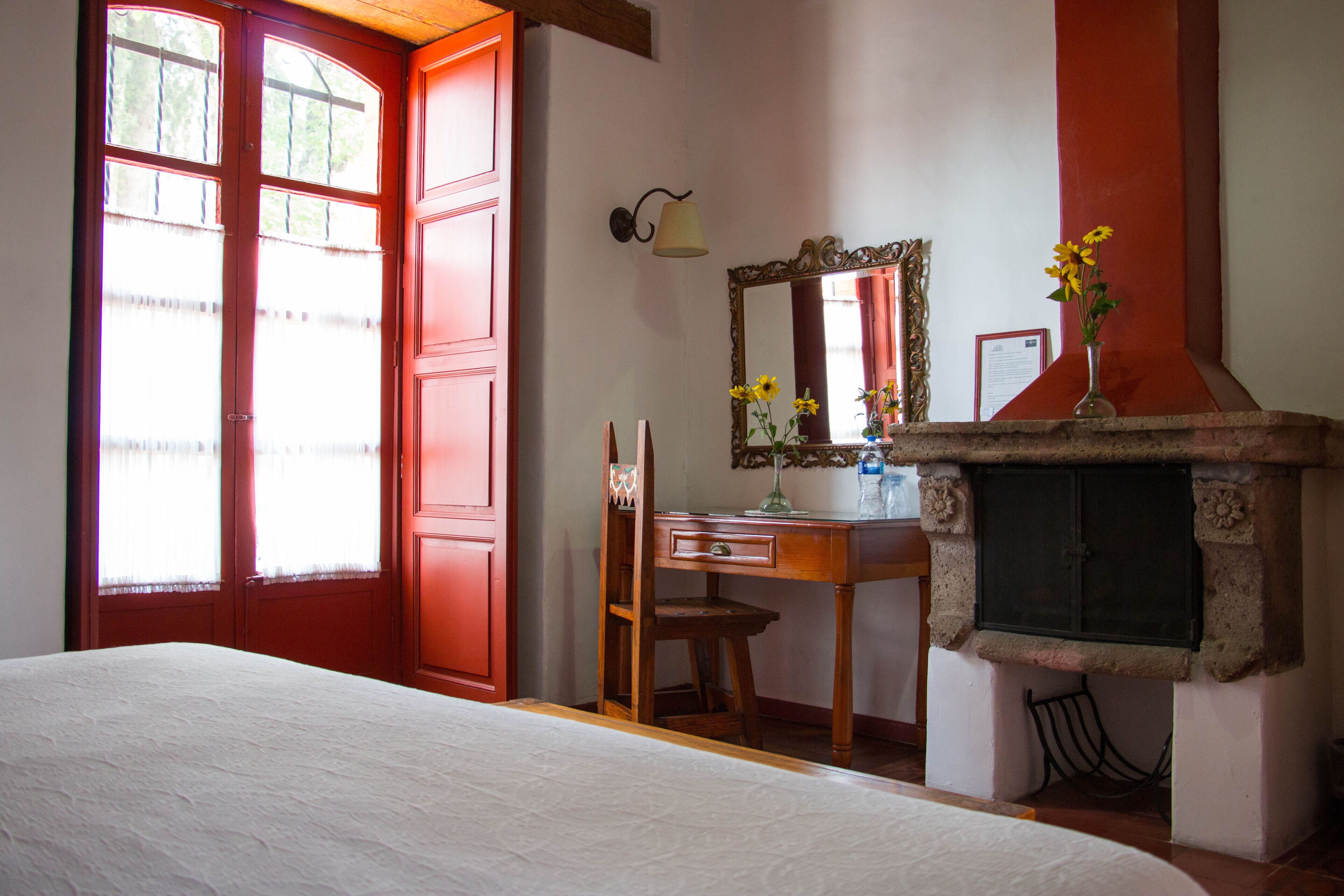 Une chambre à coucher avec un lit, un bureau en bois, une chaise, un miroir et une cheminée.