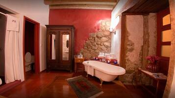 A bathroom with a clawfoot bathtub, a wooden cabinet, and a stone wall.